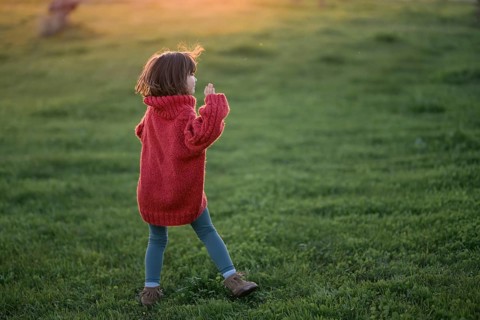A young girl, wearing a cozy red sweater and blue pants, wanders through a lush green field during