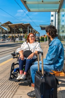 Woman in a wheelchair chatting with a tourist at a tram stop, enjoying the warmth of summer travel