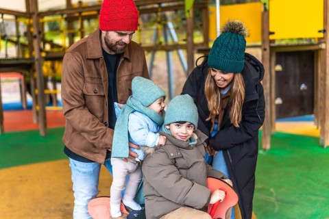 Smiling family enjoying a winter day at the playground, playing together on a rocking horse