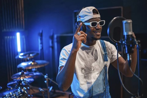 Young male singer wearing trendy white sunglasses and headphones, recording vocals for new music