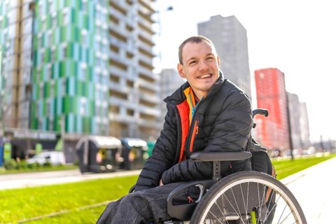 Portrait of a cheerful young disabled man in a wheelchair enjoying a sunny day in the city