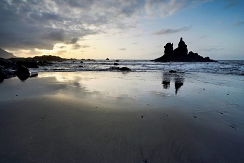 Dramatic cloudy atmosphere with rock formation at rising tide at sunset on the beach of Playa de