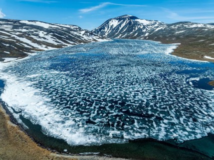 Melting ice on mountain lake Bessvatn, Mt. Besshö, old snow in early spring, aerial view,