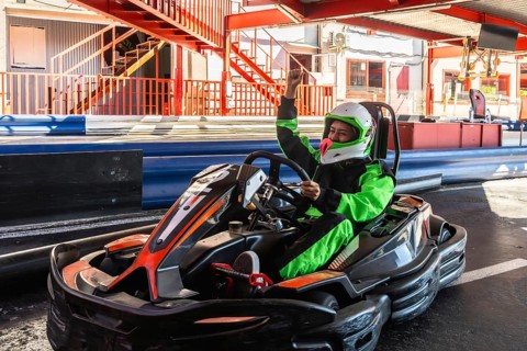 Woman kart driver wearing a helmet and green racing suit raising arm in triumph after winning a