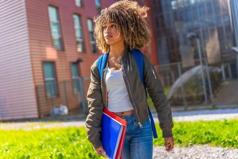 Urban female latin student with curly hair standing distracted outside the university