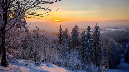 View from Döbra Berg, wide winter landscape with spectacular orange sunset with snow and trees,