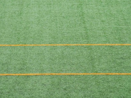 Close up view of green artificial turf featuring parallel yellow lines. Ideal for soccer fields,