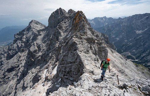 Mountaineer with helmet climbing in a secured climb on the rock, on a narrow rocky ridge, crossing