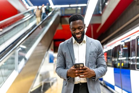 Smiling businessman using a smartphone while waiting for a train at an urban subway station,