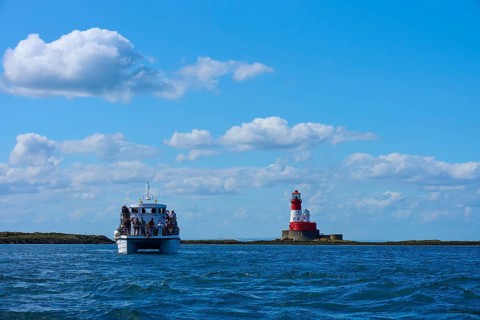 Passenger ship at sea near a red and white lighthouse under blue sky, Seahouses, Longstone