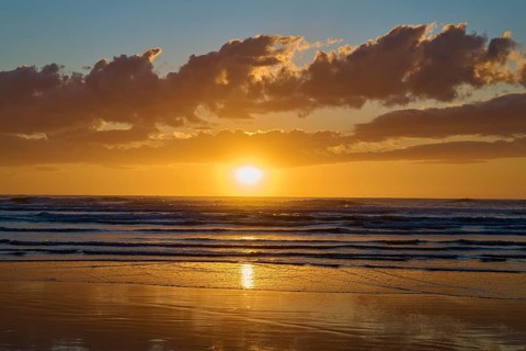 Warm sunlight hits the sea under dramatic clouds during sunrise, Muriwai Beach, Auckland, North
