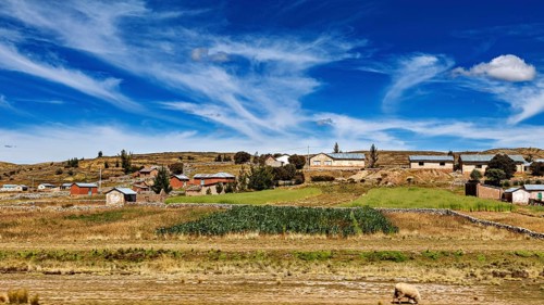 Green and brown fields with small houses under a lively sky, the villages and countryside near Puno