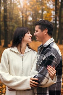 A couple shares a joyful embrace surrounded by vibrant autumn foliage in a serene forest. The warm