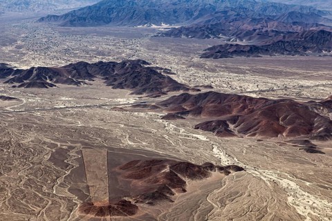 Aerial photo shows desert landscape with mountain ranges and mysterious lines on sandy soil, the