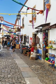 Picturesque alley with shops and pedestrians, tourists in the medieval village of Óbidos, Portugal