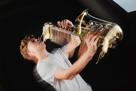 A teenage boy is captured in a dramatic pose while playing a saxophone against a black background