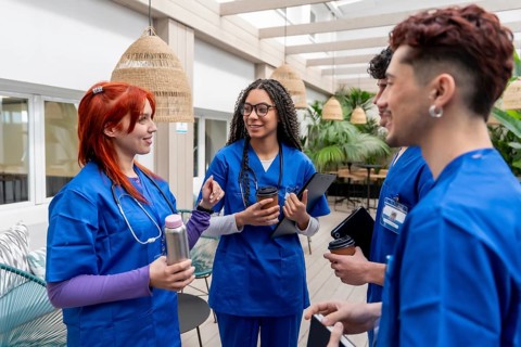 Group of diverse healthcare students in blue scrubs standing together, smiling and conversing while
