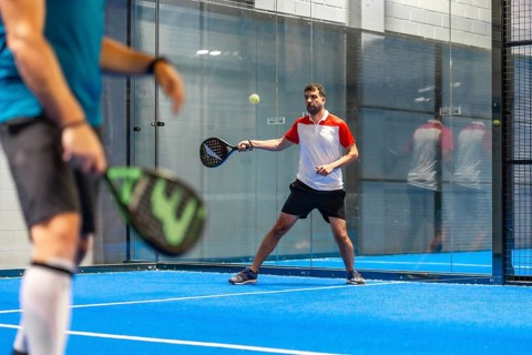 Two mature male friends playing paddle tennis in an indoor blue court