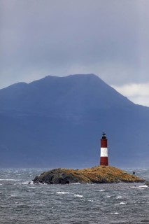 Lighthouse on a small rocky island in front of a cloudy mountain background, The lighthouse in the