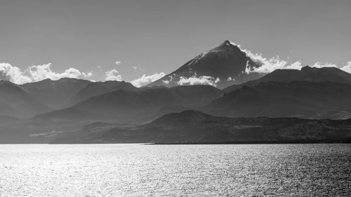 Black and white photograph of Lake Huechulafquen with the Lanin volcano against the light, Lanin