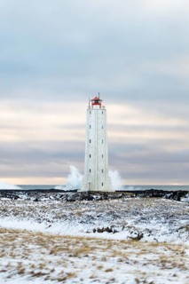 A solitary lighthouse stands resilient amidst the snowy landscape of Iceland. The scene captures