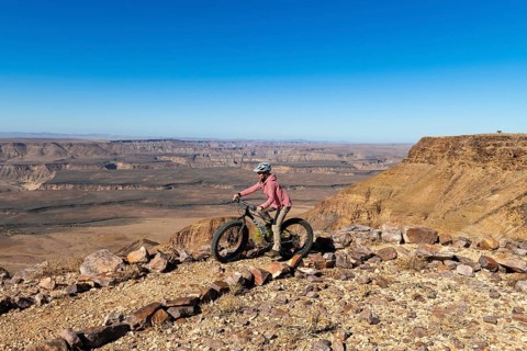 Woman riding a mountain bike, fatbike, on the edge of the abyss, behind the gorge landscape of the