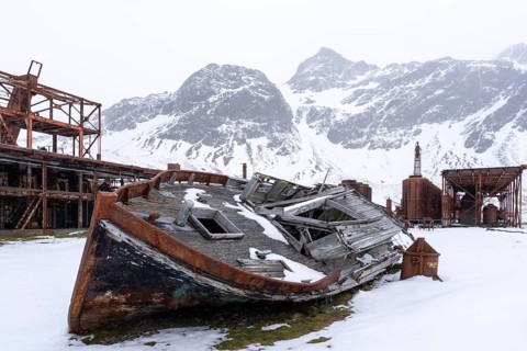 Wreck of a wooden whaling boat in front of rusted facilities of the former whaling station,