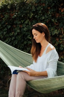 Woman quietly reading a book in a green hammock, surrounded by lush vegetation, showcasing a serene