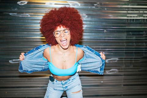 African descendent woman with vibrant afro hair expressing joy, wearing a blue bralette and denim