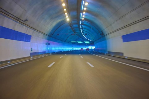 Modern, well-lit motorway tunnel with blue illuminated walls and a clear asphalt road, Zurich,