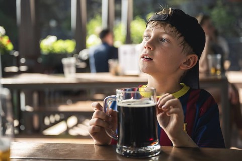 Cute boy is drinking a black drink from a large mug at a restaurant outdoor table