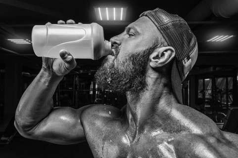 Muscular man in the gym drinking from a shaker. Fitness and bodybuilding concept.