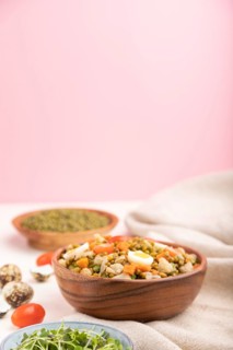 Mung bean porridge with quail eggs, tomatoes and microgreen sprouts on a white and pink background