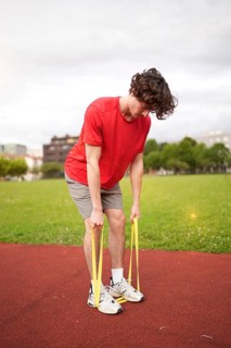 Vertical photo of a young caucasian man warming up with resistance elastic band outdoors in a