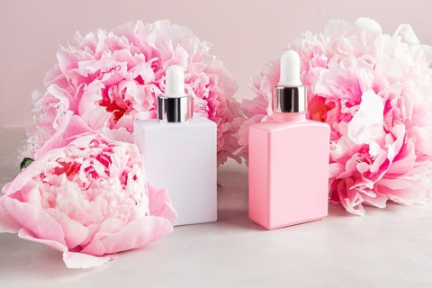 Minimalist cosmetic bottles in pink and white are elegantly placed among lush blush peonies. The