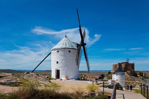 A white windmill in a sunny, rural landscape under a bright blue sky with a few clouds, Consuegra,