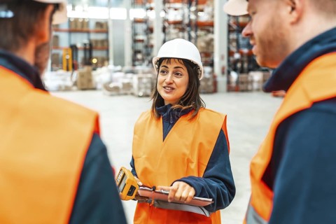 Female supervisor holding barcode scanner and clipboard briefing warehouse workers about their