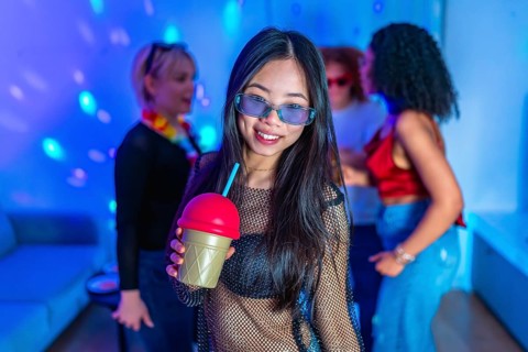 Asian woman holding a colorful slushy drink, smiling and enjoying the vibrant atmosphere of a