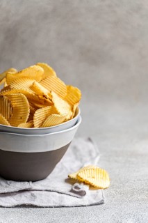 A bowl filled with golden homemade chips is set against a rustic background on a light fabric. The