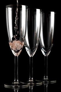 Three champagne glasses in front of a black background, first glass is filled with champagne