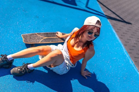 Top view of a distracted young asian woman in denim clohtes sitting next to skateboard in a park