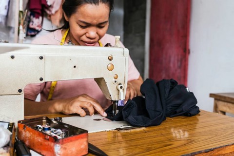 A asian seamstress deeply focused, meticulously sewing fabric with a sewing machine in a vibrant