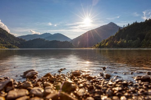 Peaceful lake with mountain backdrop, golden sky and sunlight on water and stones, Weitsee