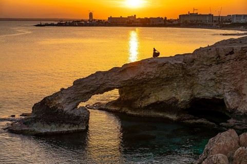 Young woman on the natural rock bridge Love Bridge in the sunset, Agia Napa, Cyprus