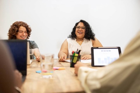 A multiracial group collaborates at a coworking space, engaging in a lively discussion. Laptops and