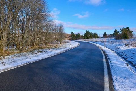 A winding road leads through a snow-covered landscape with trees and a clear blue sky, winter,