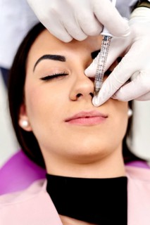 A close-up image of a cosmetic facial procedure, showing a professional administering an injection