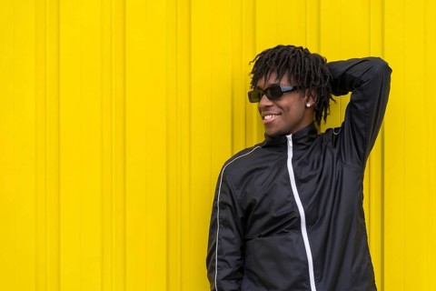 Cool young african man posing relaxed outdoors next to an urban yellow background