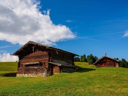 Alpine huts on green meadows, spring clouds above, Alpe di Siusi, Dolomites, South Tyrol, Italy