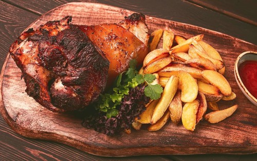 Pork knuckle, in soy-honey sauce, with fried potatoes, on a wooden chopping board, homemade, no